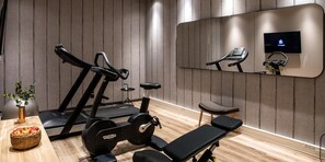 Une salle de sport équipée de matériel d’exercice, d’un banc, d’un miroir et d’un téléviseur fixé au mur.