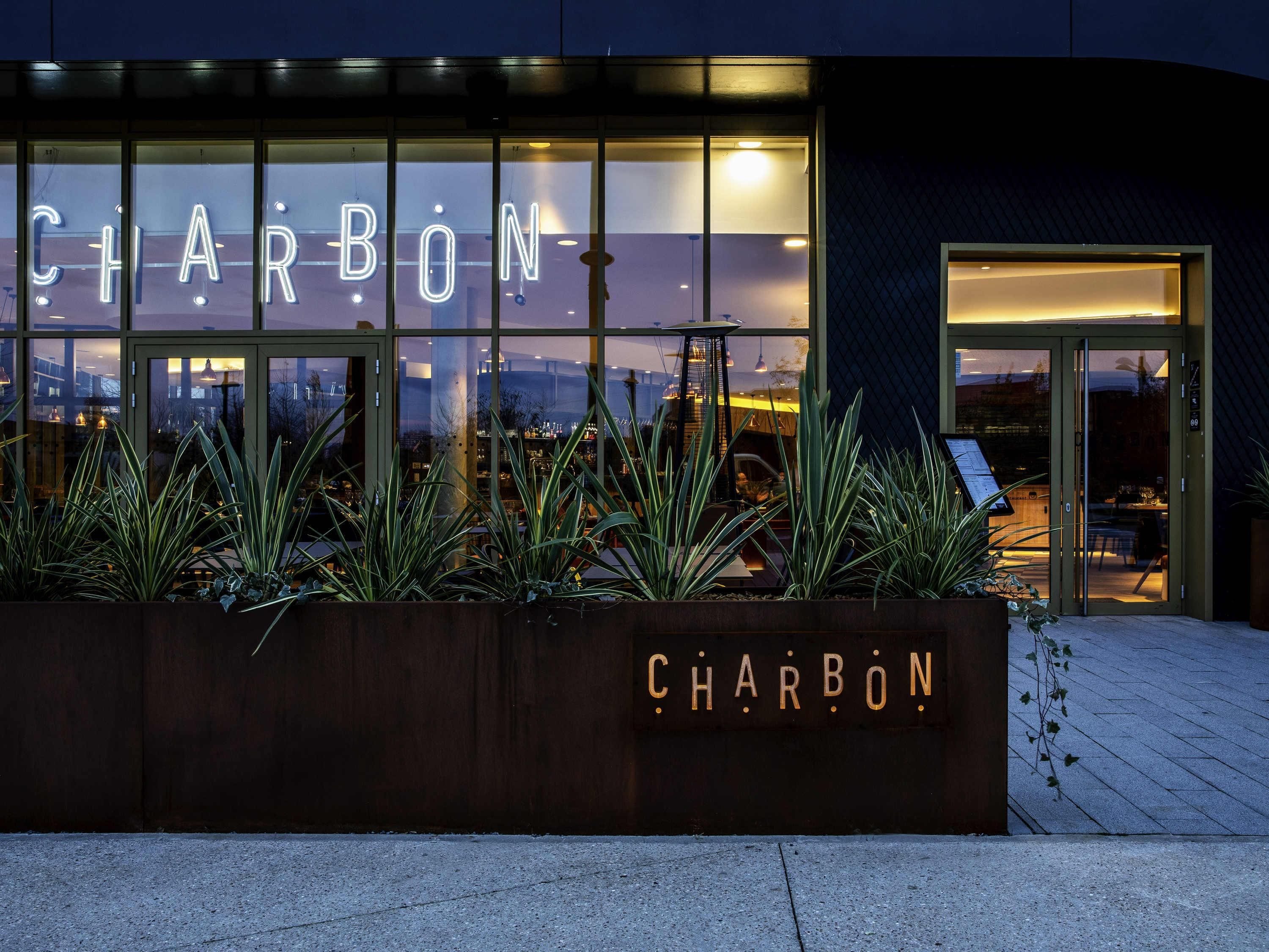En byggnad med en stor, upplyst skylt som visar ordet ”CHARBON” och en fasad av glas.