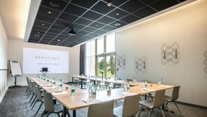 Een vergaderzaal met een lange tafel, stoelen, een projectiescherm en een presentatie over Mercure Hotels Parijs.