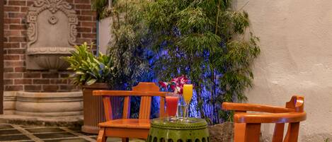 A patio with wooden chairs and a table, a potted plant, and a decorative wall.