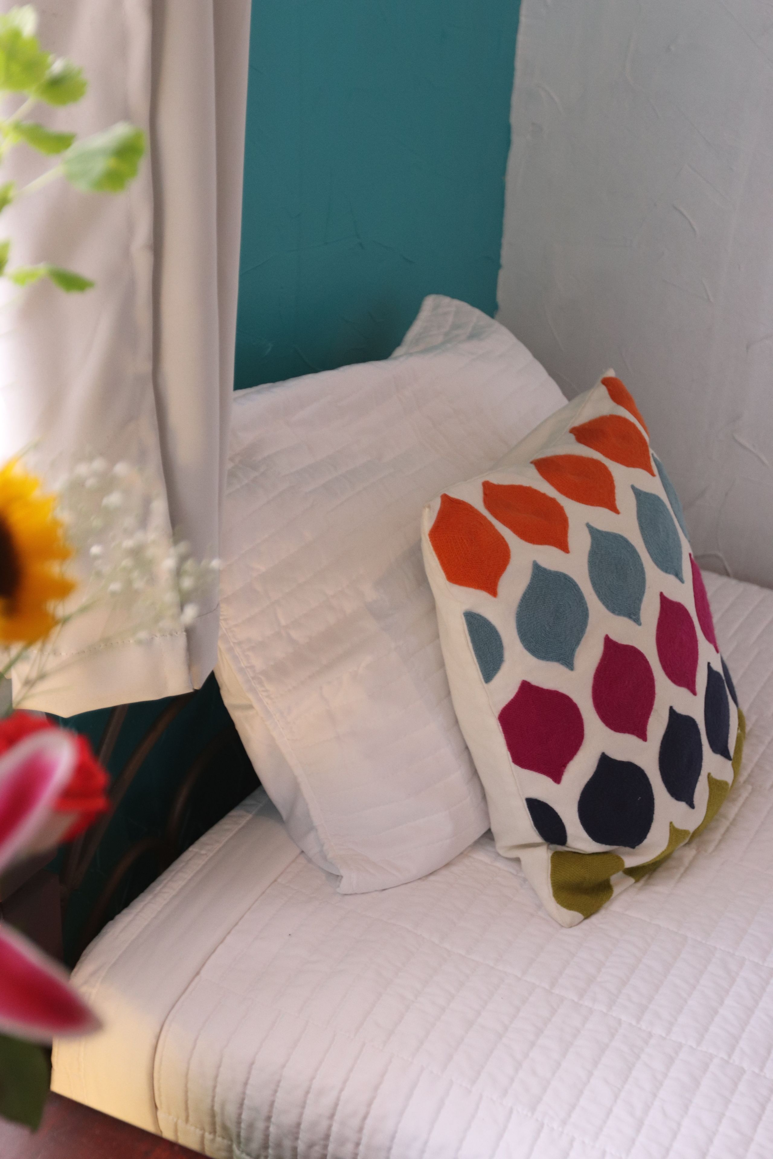 A bed with a white quilt and a colorful pillow with a geometric pattern.