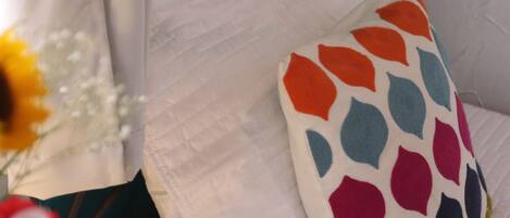 A bed with a white quilt and a colorful pillow with a geometric pattern.