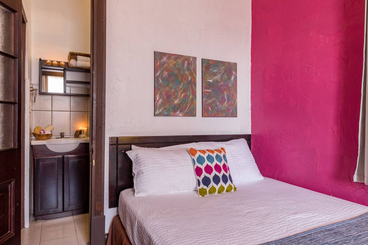 Un dormitorio con cama, mesita de noche, cómoda y una pared decorada con dos cuadros abstractos.