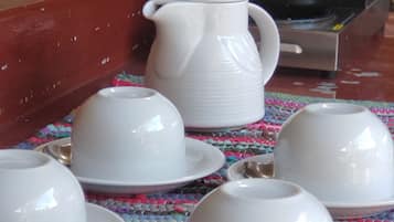 Une table avec des tasses blanches et un pichet, une machine à café Bunn et un tapis coloré en fibres tressées.