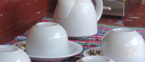 A table with white cups and a jug, a Bunn coffee maker, and a colorful woven mat.