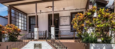 Un hôtel doté d’une entrée couverte, d’un escalier menant au bâtiment principal et d’une enseigne indiquant qu’il s’agit de l’hôtel Alajuela City.