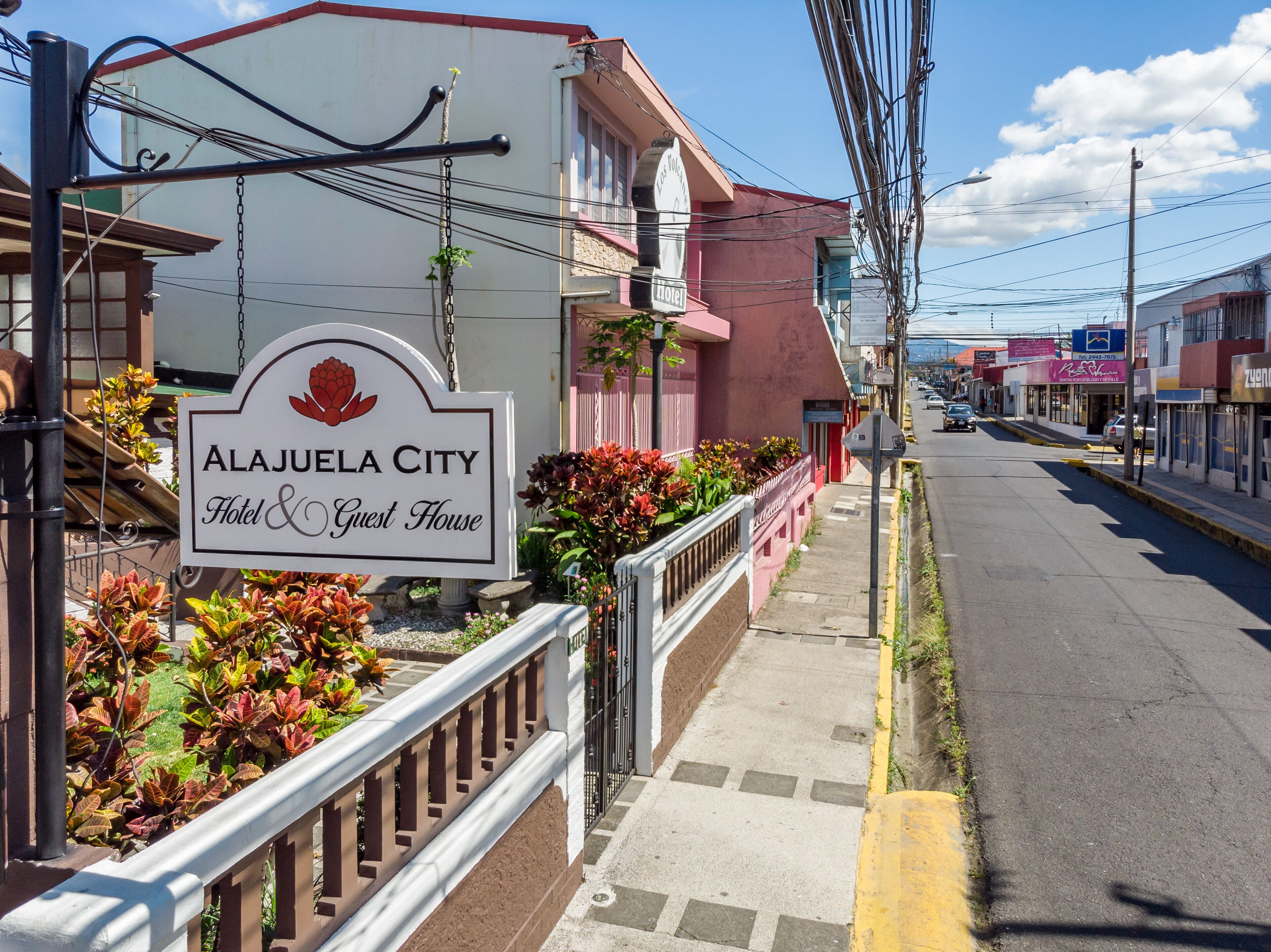Ein Hotelschild mit einem roten Blütenlogo und dem Namen "Alajuela City Hotel & Guest House".
