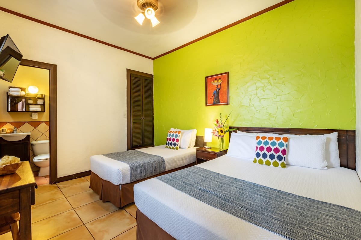 Una habitación de hotel con dos camas, baño, escritorio y mesita de noche con lámpara.