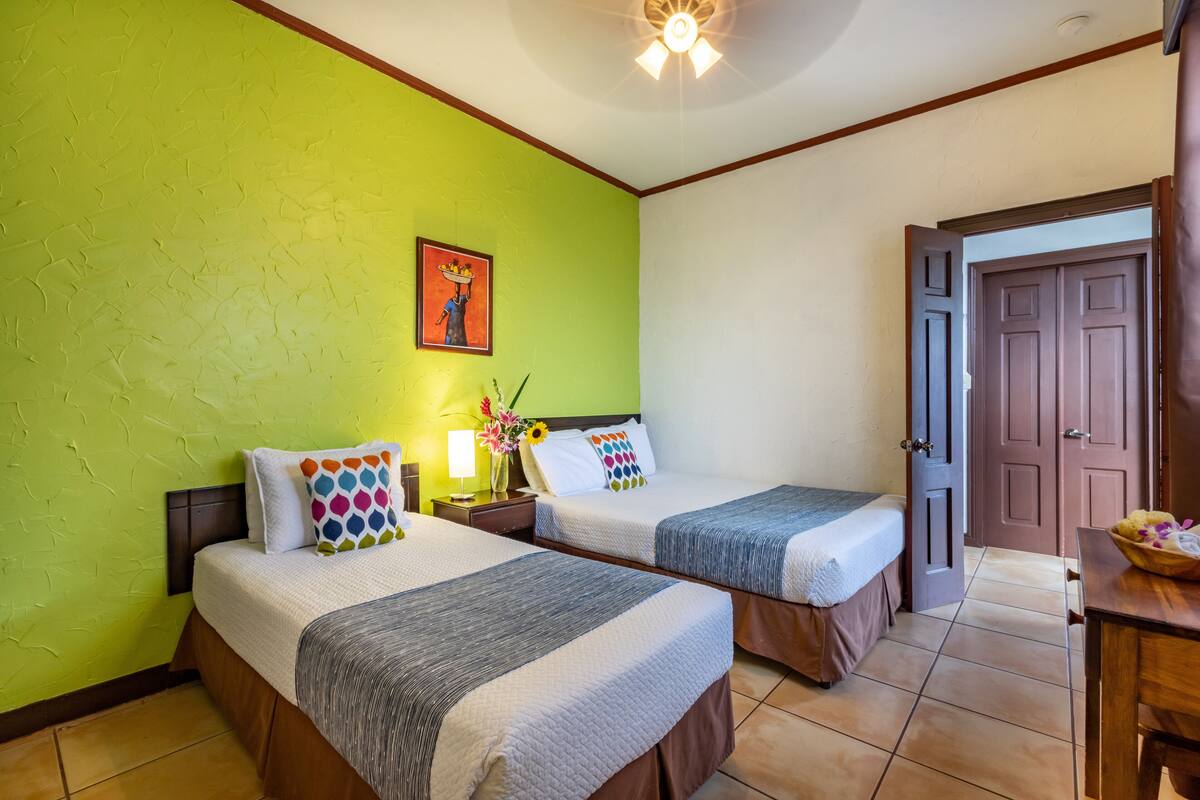 Una habitación de hotel con dos camas, una pared verde, un cuadro y una puerta de madera.