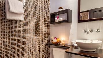 A bathroom with mosaic tile walls, a white toilet, a sink with a mirror, and a shelf with toiletries.