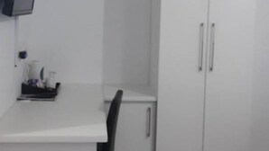 Uma cozinha compacta com armários brancos, uma pequena mesa de jantar e uma TV fixada na parede.