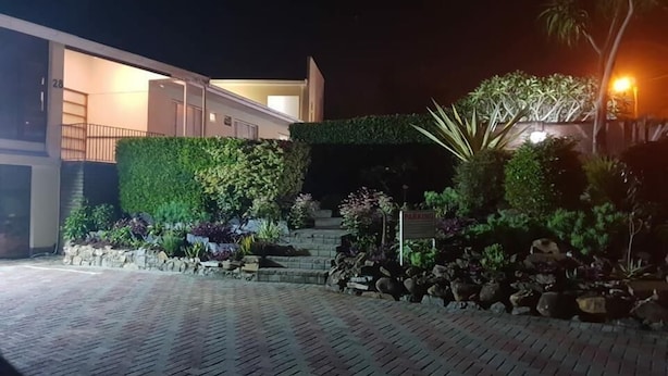 Um edifício moderno com entrada bem iluminada, um caminho de acesso pavimentado e um jardim ajardinado com diversas plantas e um pequeno jardim de pedras.