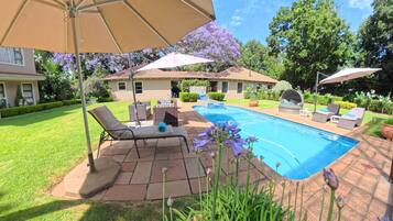 A backyard with a swimming pool, patio furniture, and a covered seating area.