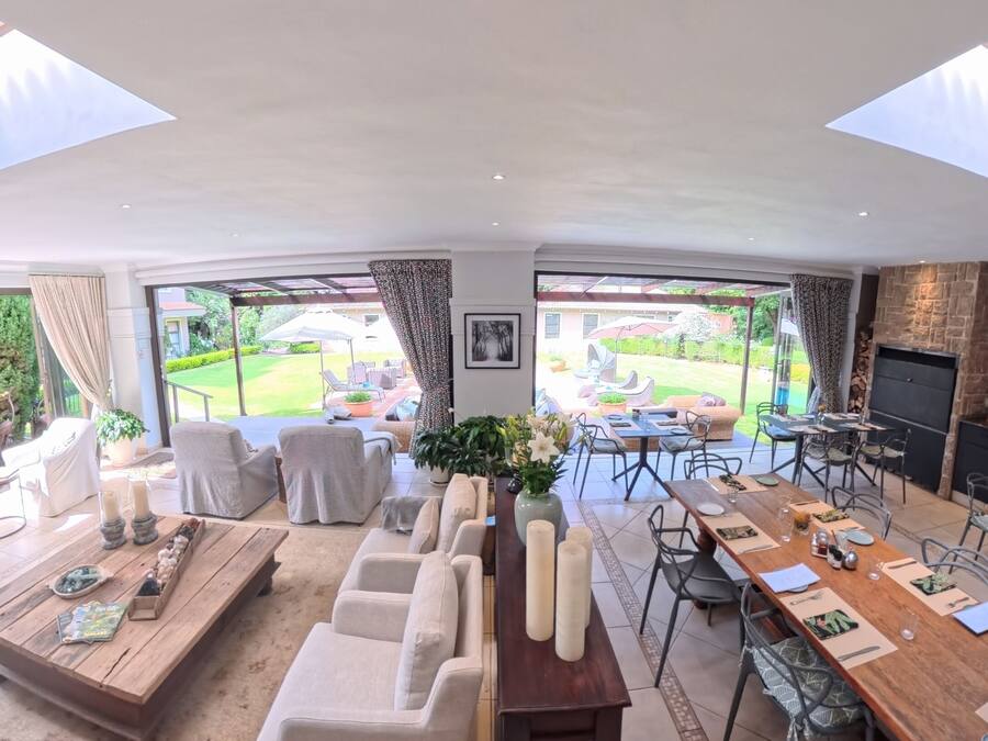 Un vaste espace de vie comprenant une table à manger, des canapés et une cheminée. De grandes fenêtres offrent une vue sur un jardin.