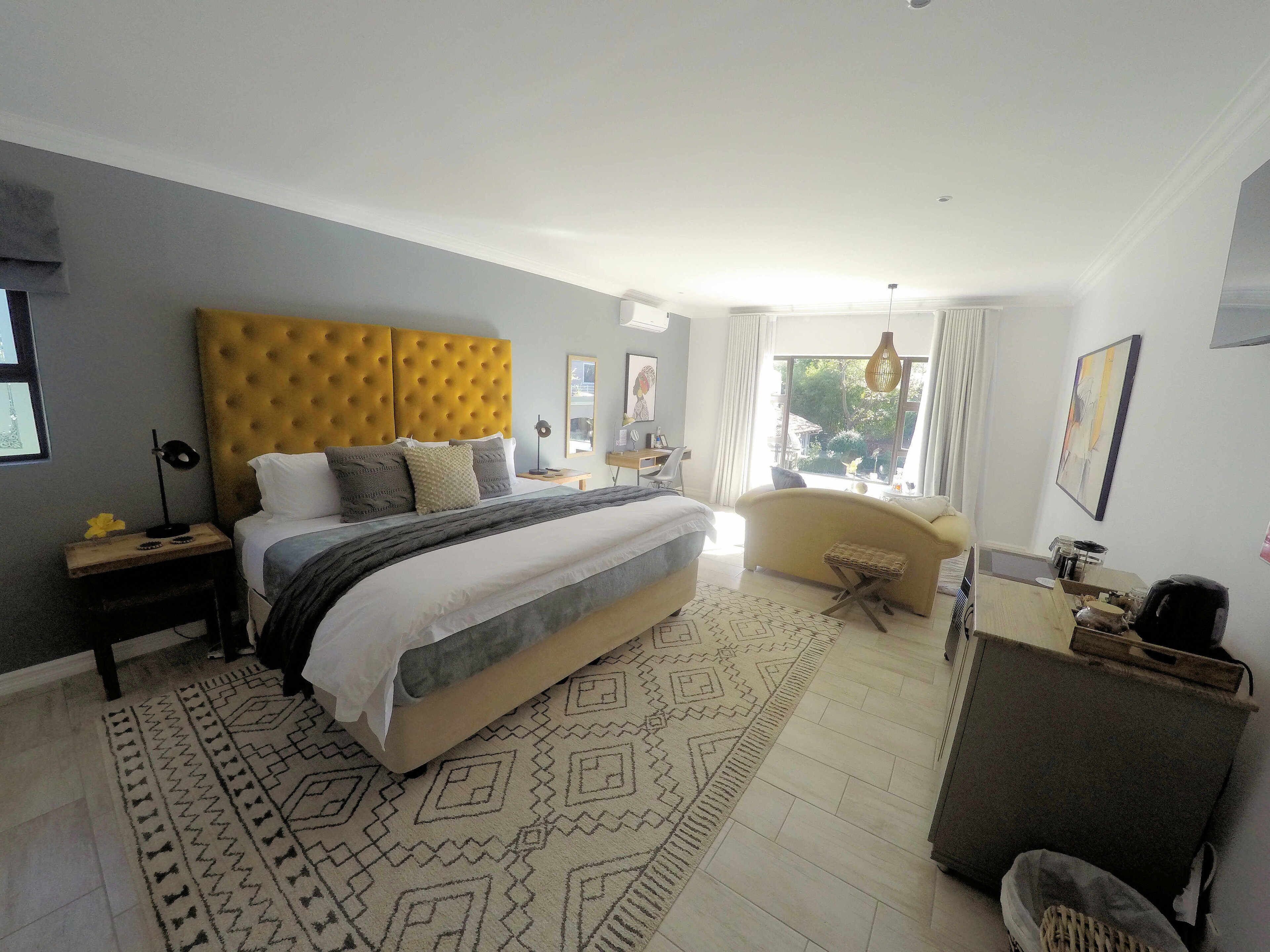 A modern bedroom with a large bed, a sofa, a desk, and a view of the outdoors.