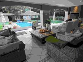 Un espacio de estar al aire libre cubierto con mobiliario de mimbre, una piscina y una casa al fondo.