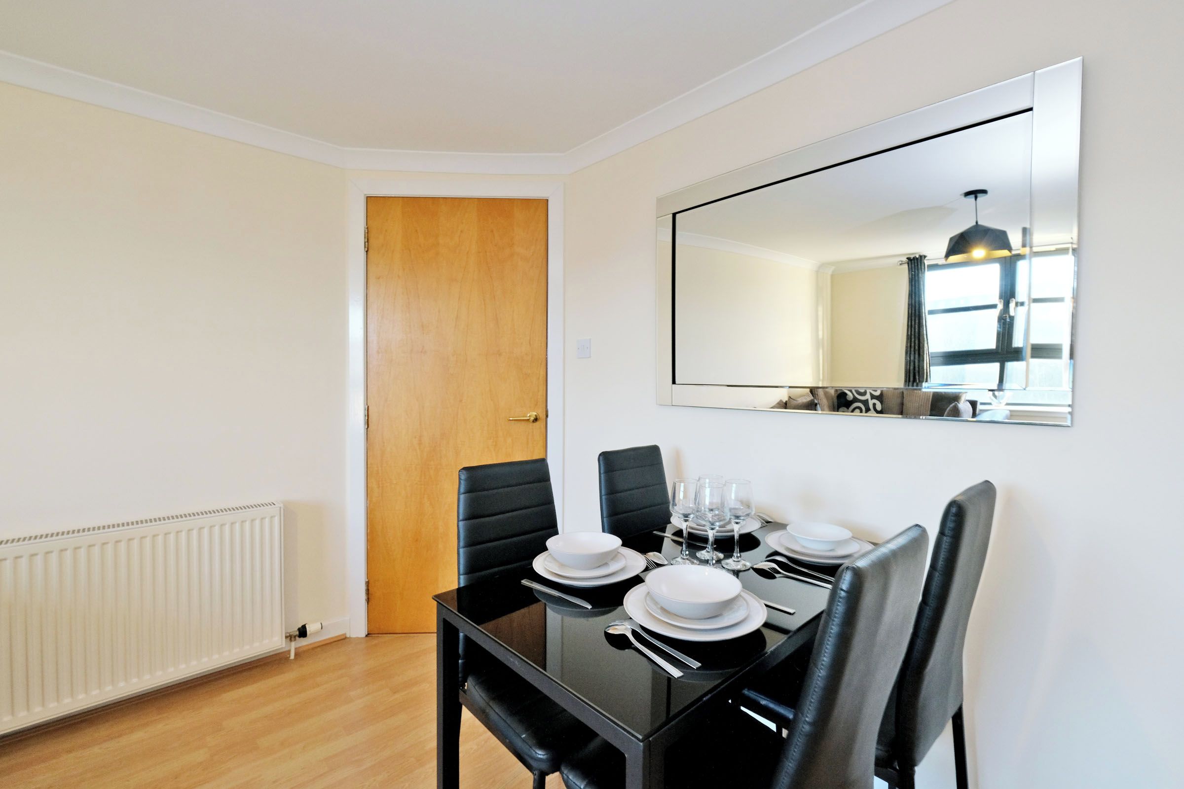 A dining area with a table set for four, a mirror on the wall, and a door leading to another room.