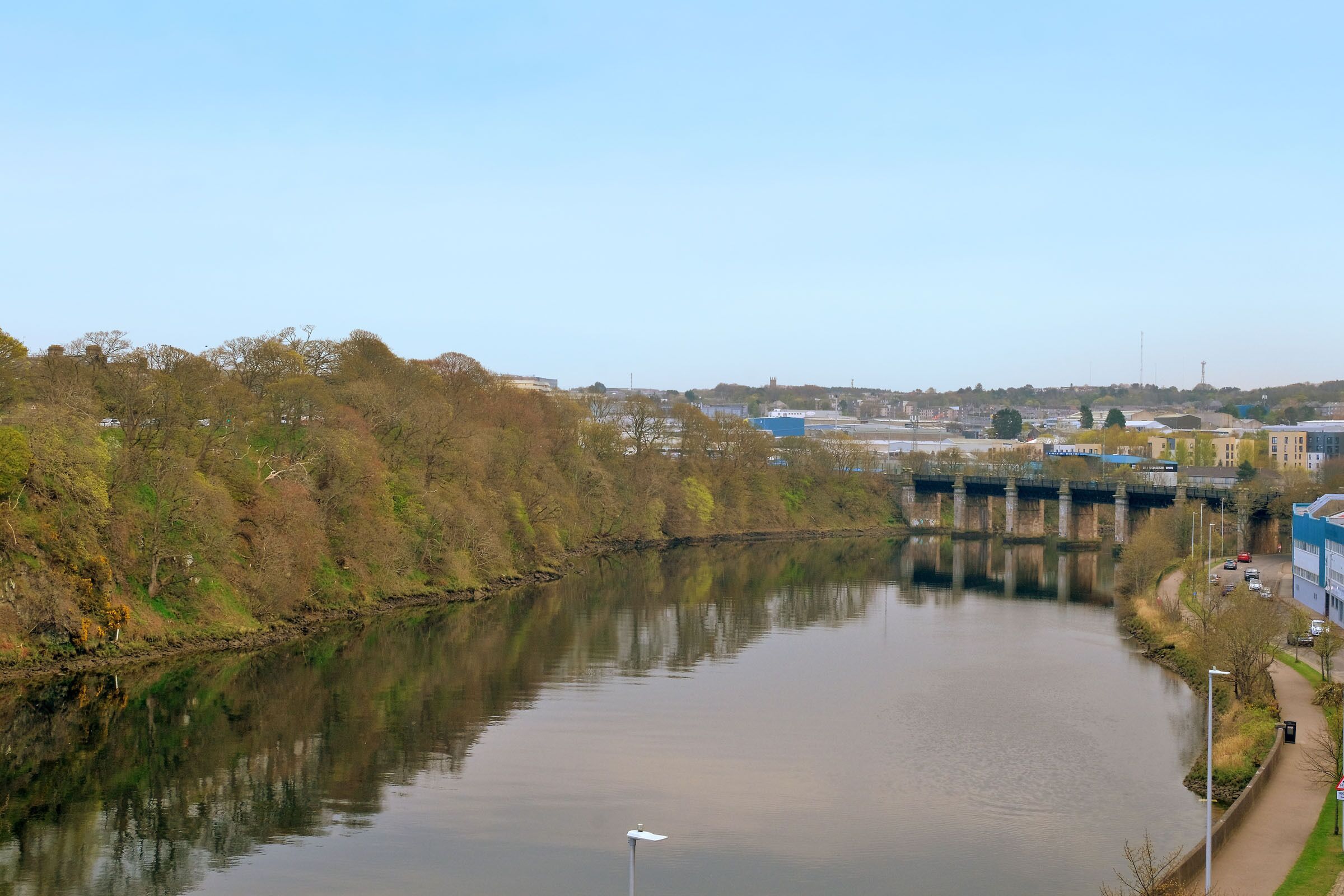 Une rivière avec un pont, des arbres et des bâtiments en arrière-plan.