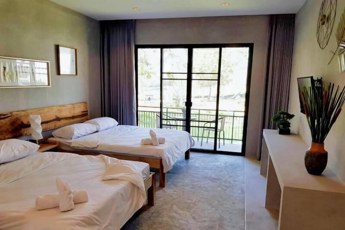 Habitación de hotel con dos camas, un balcón con vistas y un escritorio con un florero.