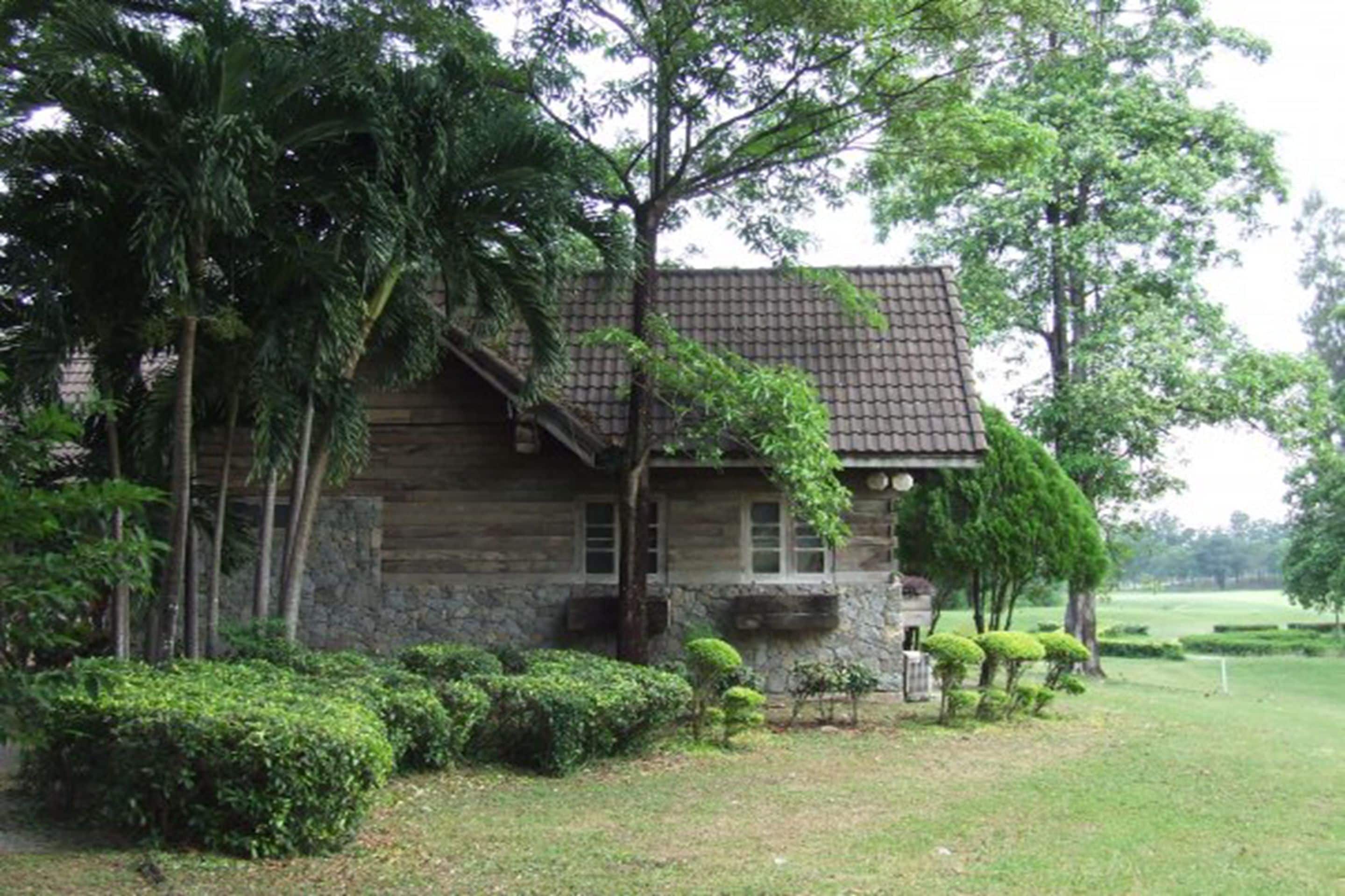 A rustic stone house with a tiled roof, surrounded by lush greenery and a well-maintained lawn.