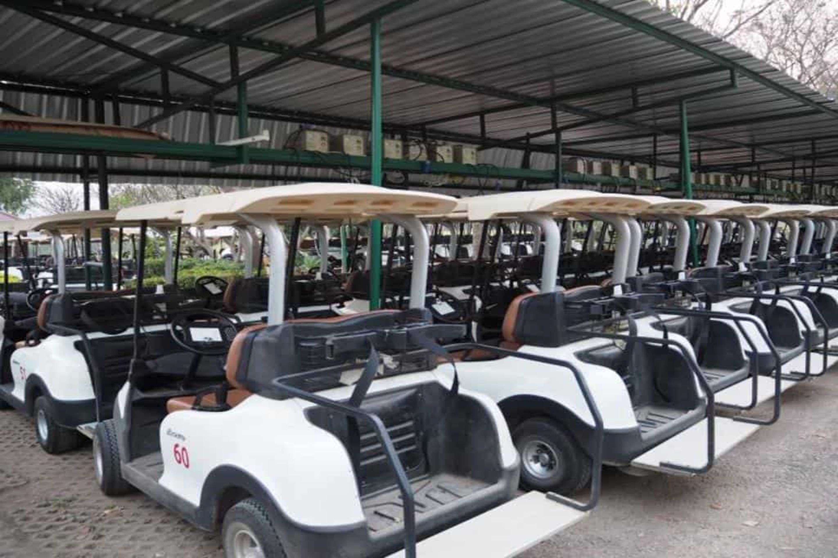 Una hilera de carros de golf estacionados bajo una zona techada con techo de metal.