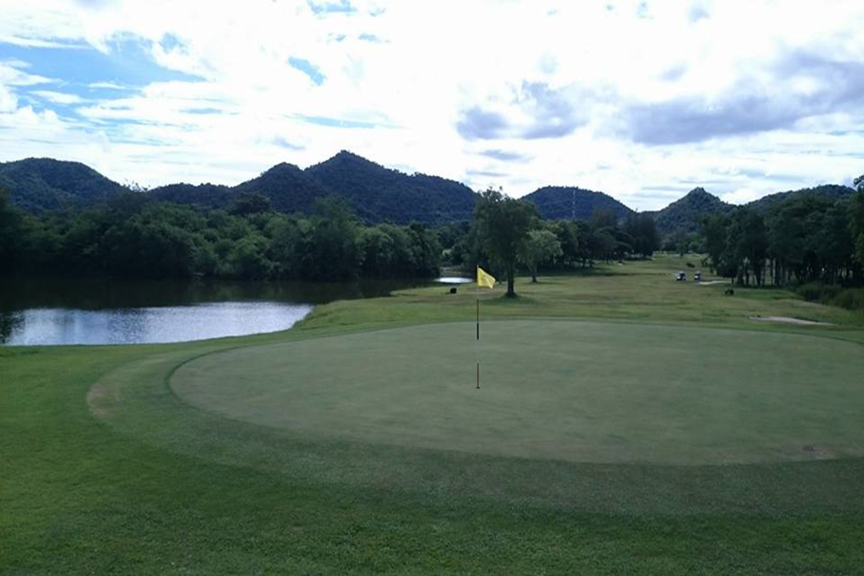 Un campo de golf con un marcador en el centro, rodeado de vegetación exuberante y un lago.