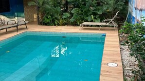 A rectangular swimming pool with tiled edges, surrounded by a wooden deck and lush greenery. - Be My Guest Cabinas (Cahuita)