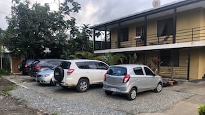 A parking area with several cars, a building with a balcony, and surrounding greenery. - Be My Guest Cabinas (Cahuita)