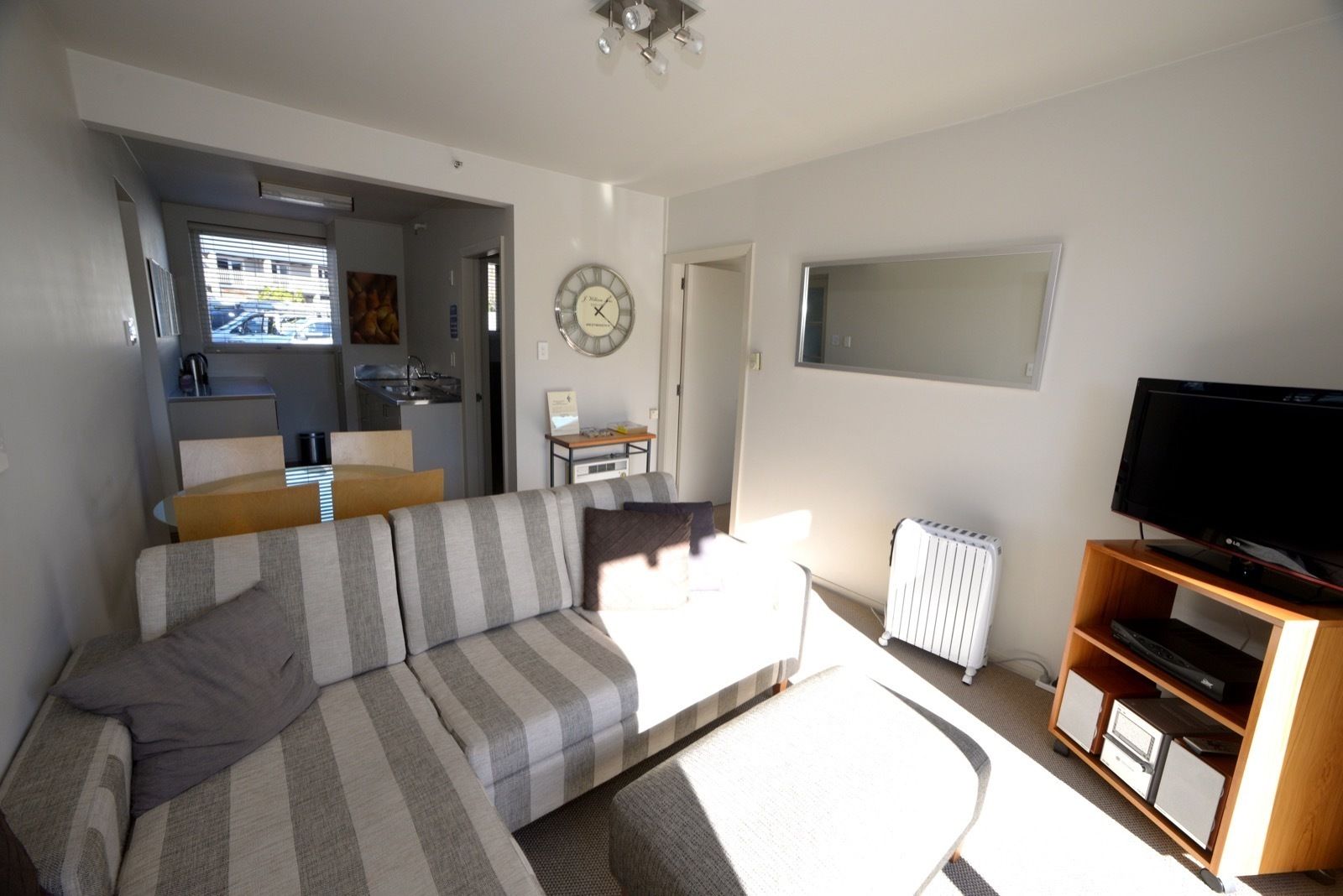 A modern living room with a striped sofa, a flat-screen TV on a wooden stand, and a dining area with a table and chairs.