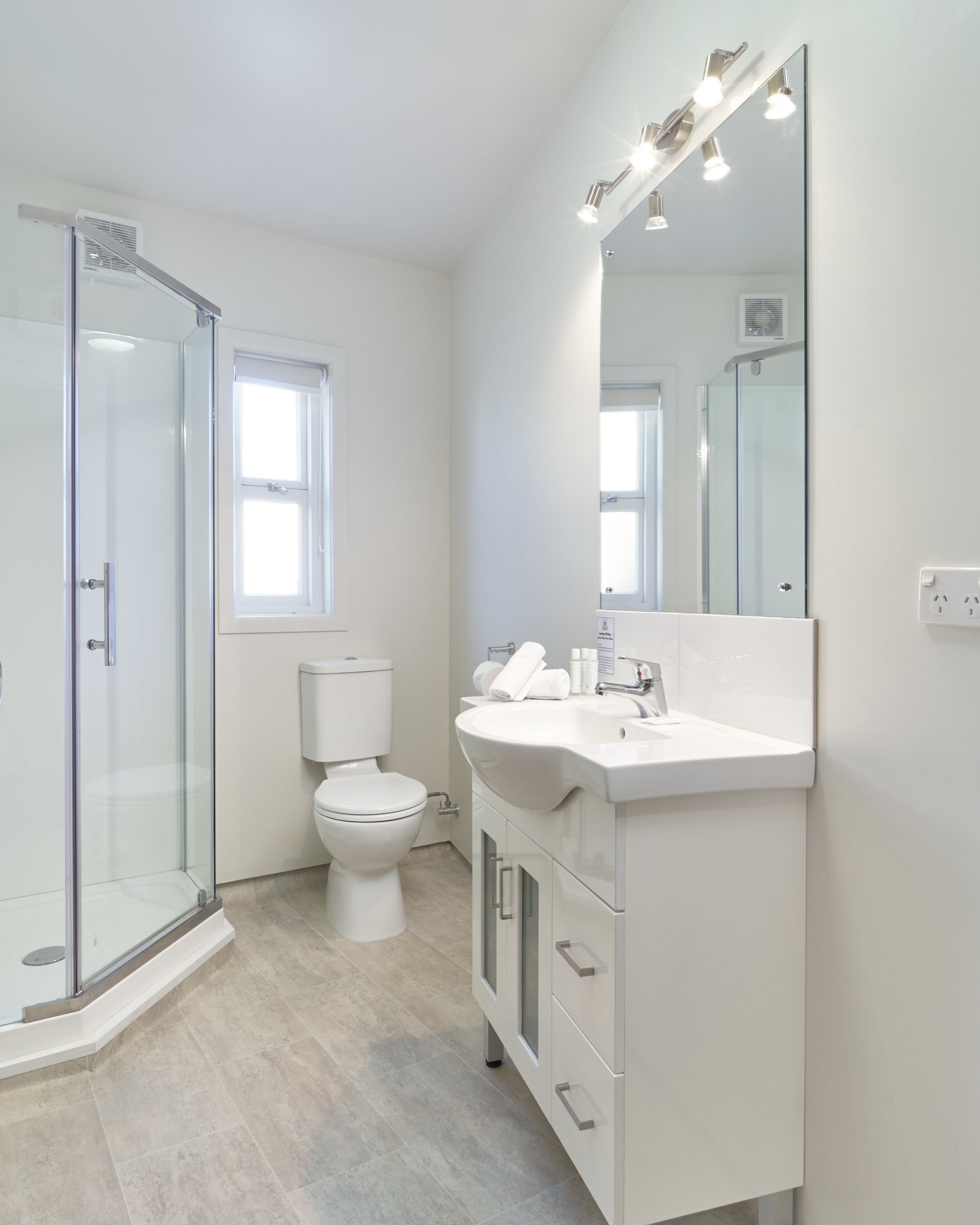 A modern bathroom with a glass shower enclosure, a toilet, and a vanity with a mirror.