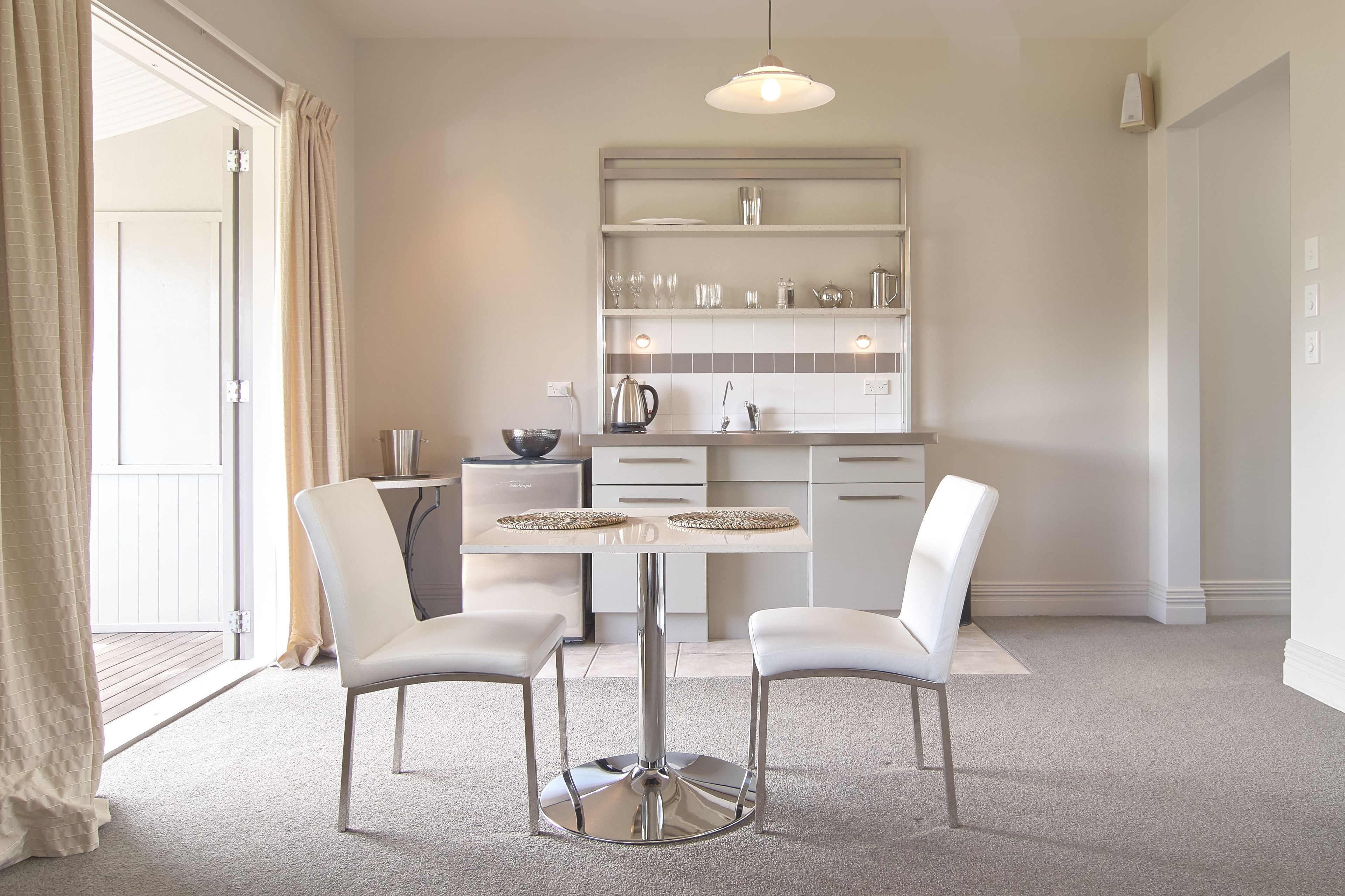 A modern kitchen with white cabinetry, a central island with two chairs, and a dining table.
