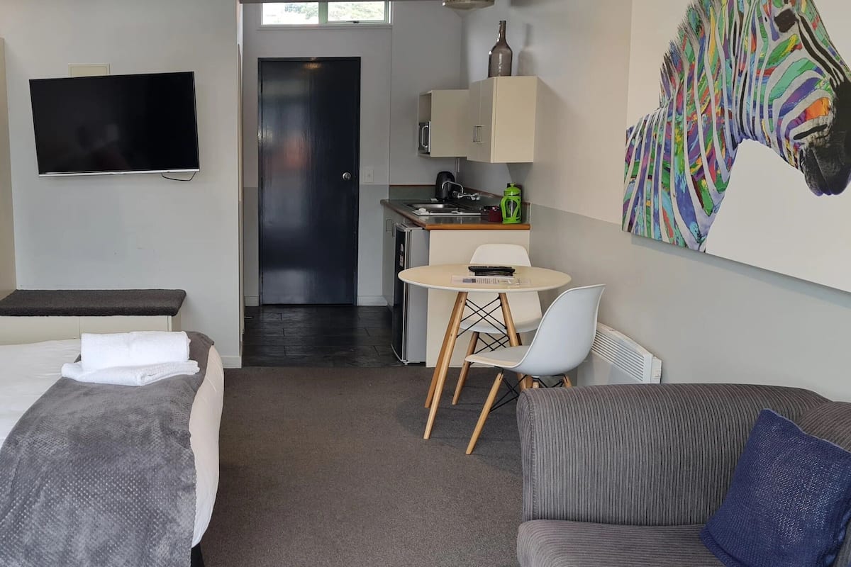 Ein Hotelzimmer mit Bett, Schreibtisch, Stuhl, Sofa, Fernseher und Küchenzeile.