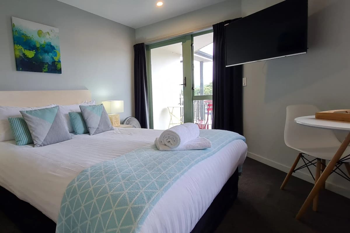 Ein Hotelzimmer mit Bett, Schreibtisch, Stuhl, Fernseher und Balkonblick.