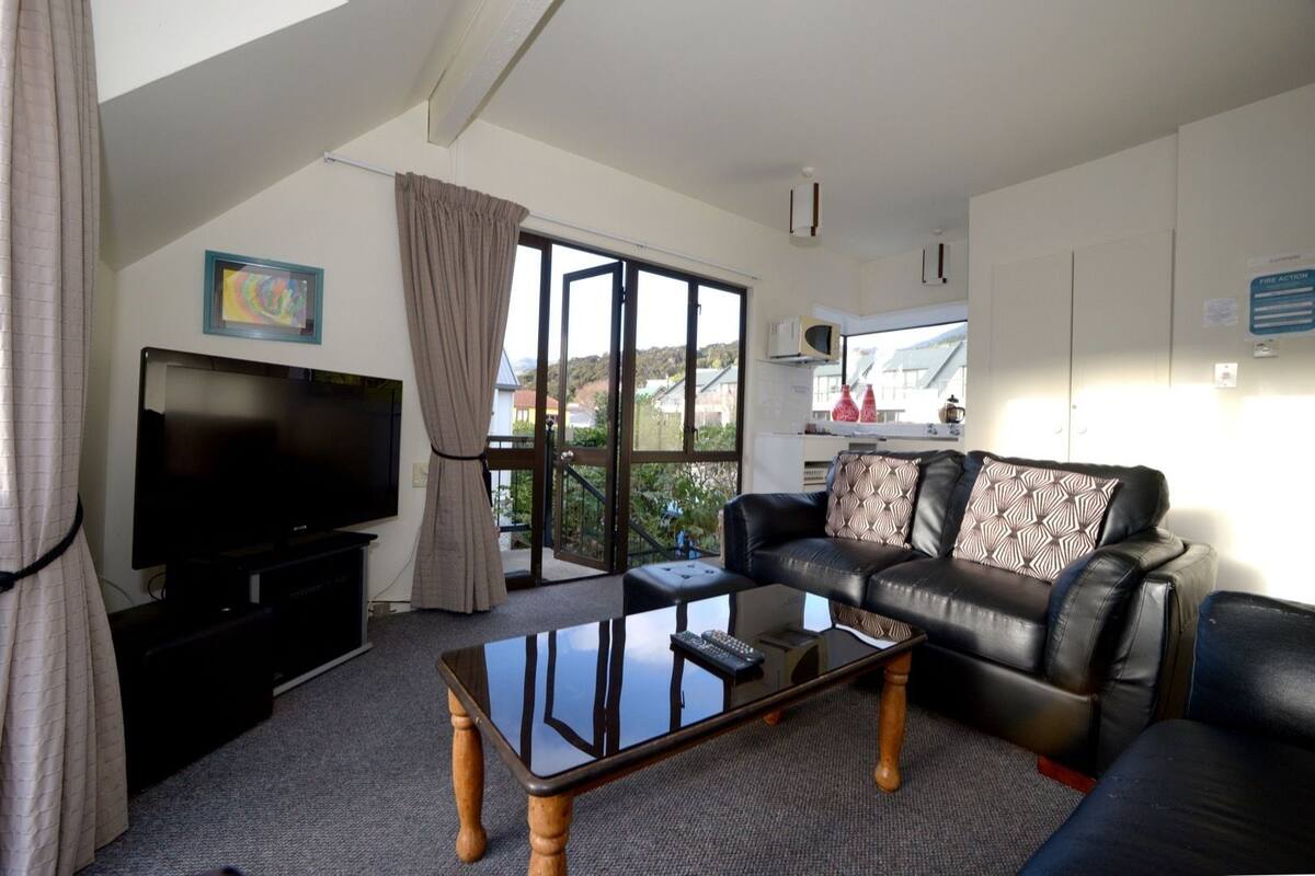 Ein Wohnzimmer mit Fernseher, Sofa und Glastisch.