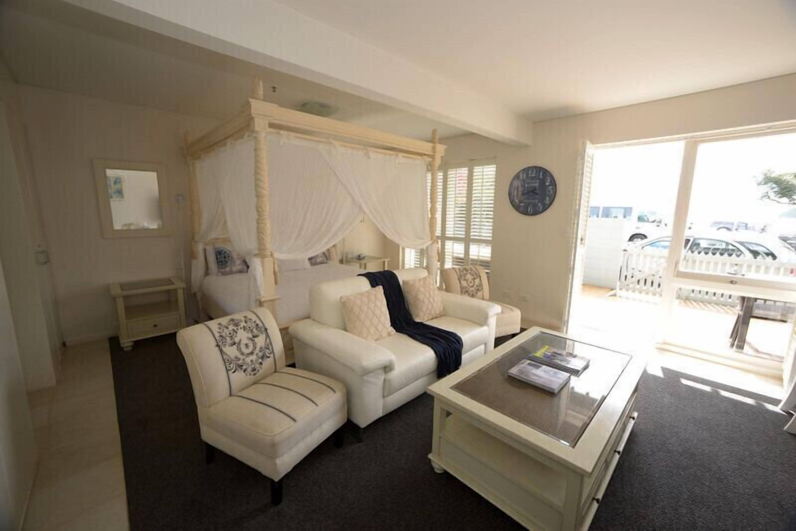 A bedroom with a four-poster bed, a sofa, a coffee table, and a view of the outside.