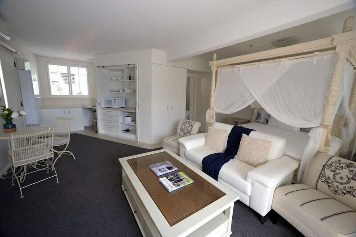 Ein modernes Wohnzimmer mit einem weißen Sofa, einem Couchtisch, einem weißen Sessel, einem weißen Kleiderschrank und einem Himmelsbett.