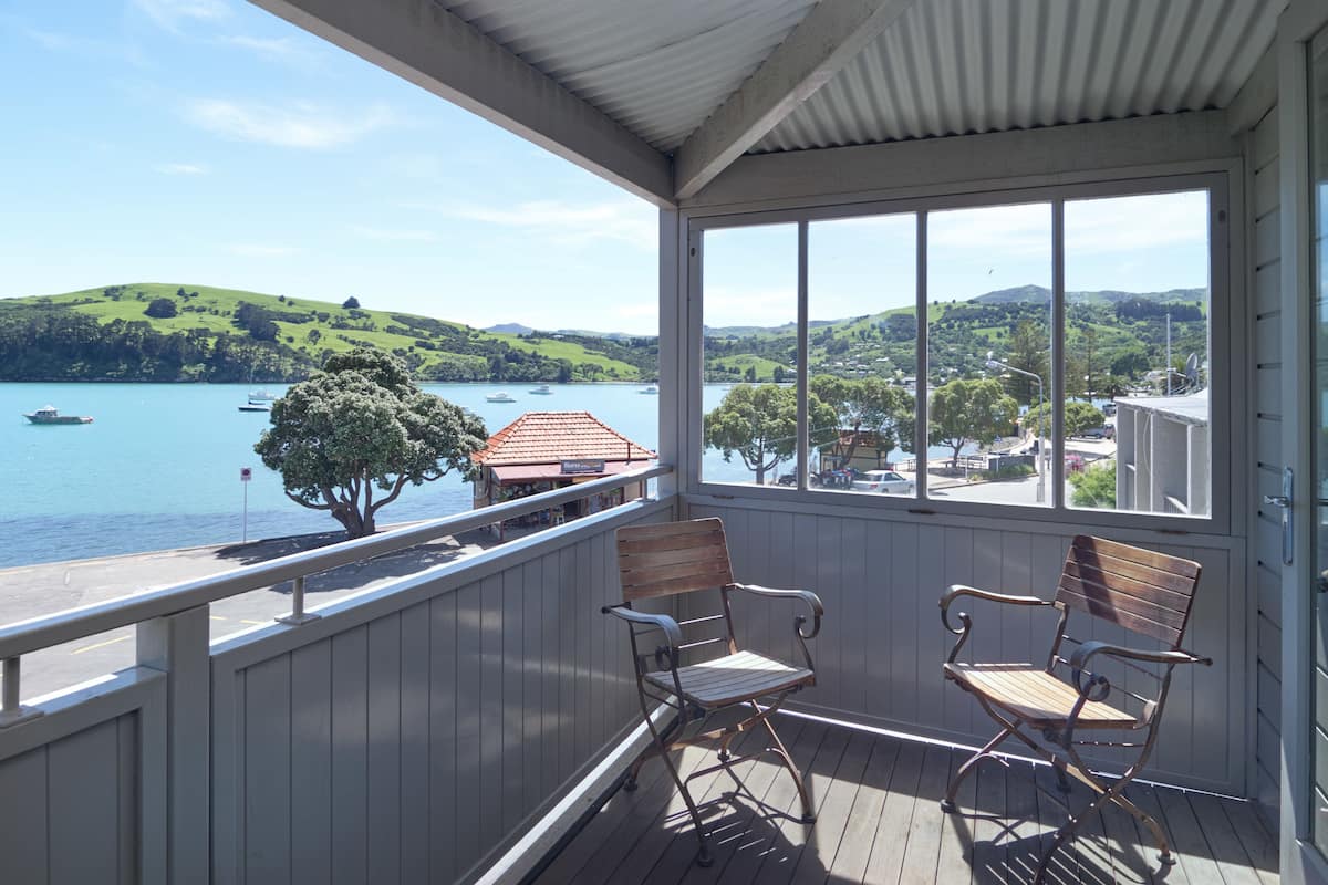 Ein überdachter Balkon mit zwei Holzstühlen, mit Blick auf einen See mit Booten und eine hügelige Landschaft.