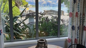 A round wooden table with a woven centerpiece, positioned by a window overlooking a marina with boats and mountains.