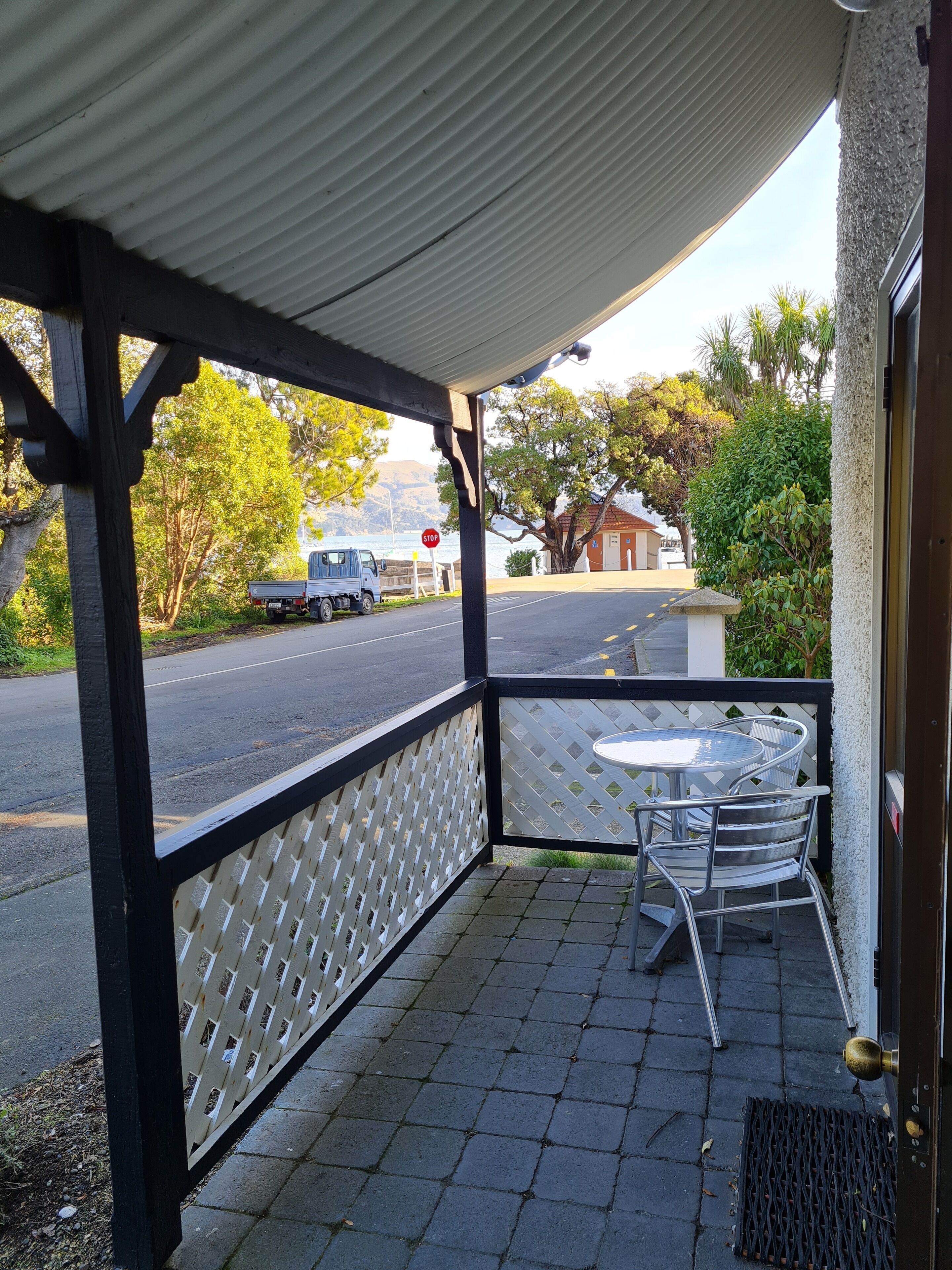 Un área de estar al aire libre con techo, una mesa y sillas, y vista a una carretera con un camión y una señal de parada.