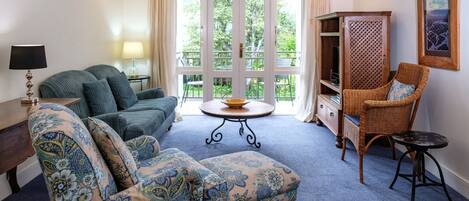 A cozy living room with a sofa, armchair, and wicker chair, a round table, and a bookshelf.