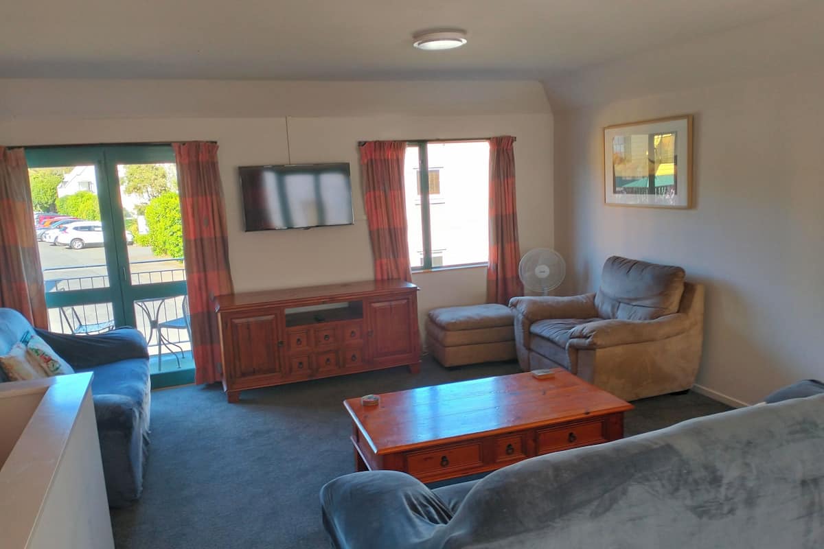 Ein Wohnzimmer mit einer Couch, einem Sessel, einem Holztisch und einem Fernseher an der Wand.