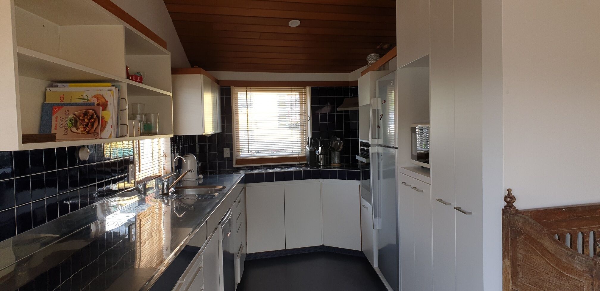 A compact kitchen with white cabinets, a black tiled backsplash, and a window with blinds.