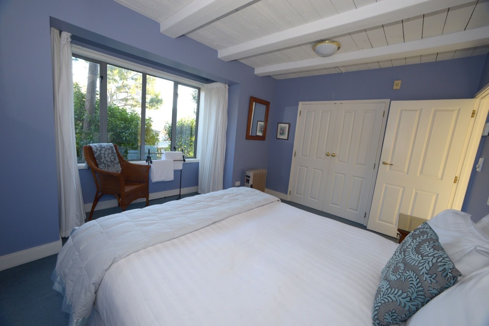Un dormitorio con una cama grande, una silla junto a la ventana y un armario.