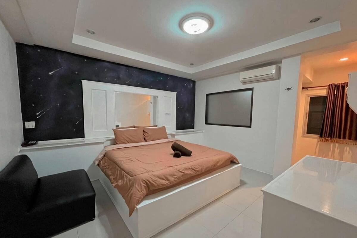 A modern bedroom with a bed, a desk, a chair, a window, and a wall-mounted TV.