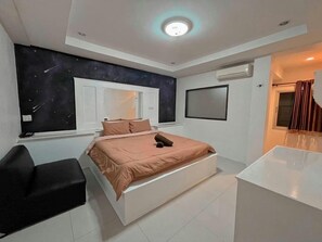 A modern bedroom with a bed, a desk, a chair, a window, and a wall-mounted TV. - Sirasit 999 Mansion (Phetchaburi)