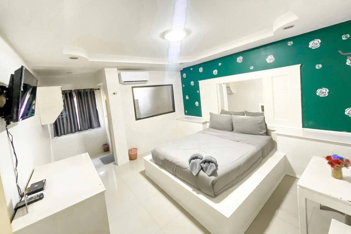 A modern bedroom with a bed, a TV mounted on the wall, a desk, and a small table with a vase of flowers.