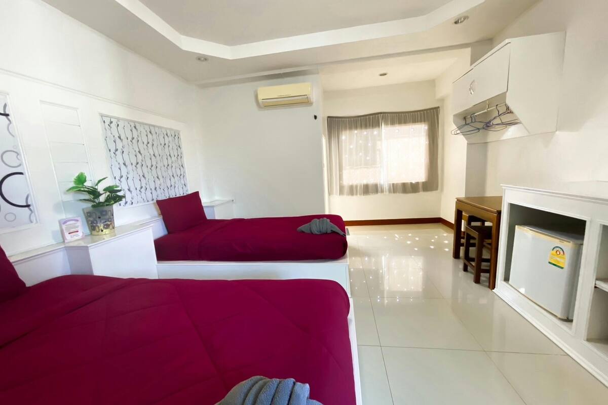 A modern hotel room with two beds, a kitchenette, and a large window with curtains.