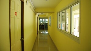 Um corredor com uma porta identificada com o número 102, uma janela com persianas e um candeeiro no teto.