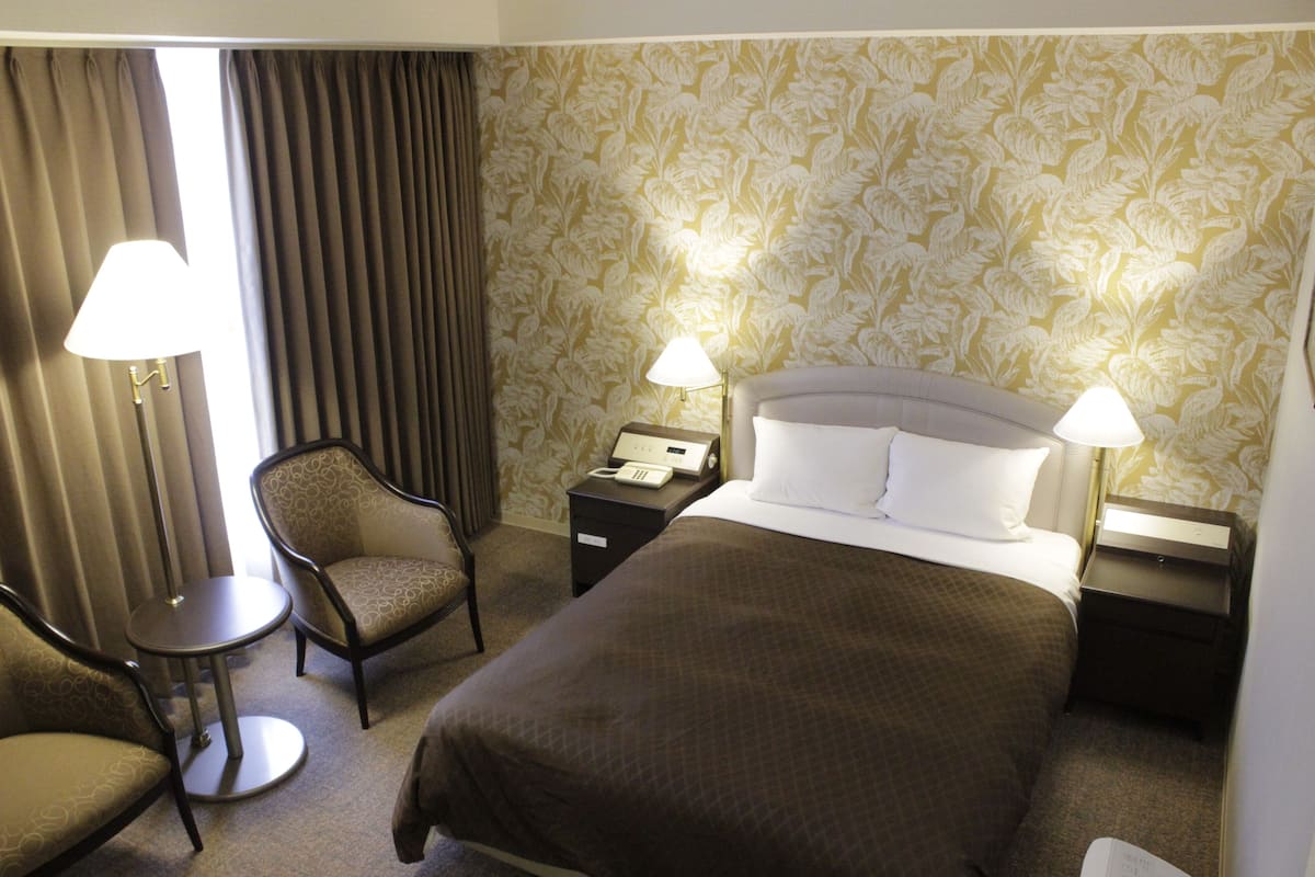 A hotel room with a bed, two bedside tables with lamps, a chair, and a small round table.
