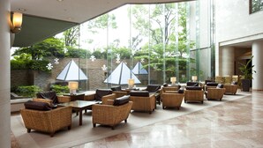 A spacious lobby with wicker furniture, large windows, and a view of greenery outside. - Rembrandt Hotel Oita (Oita)